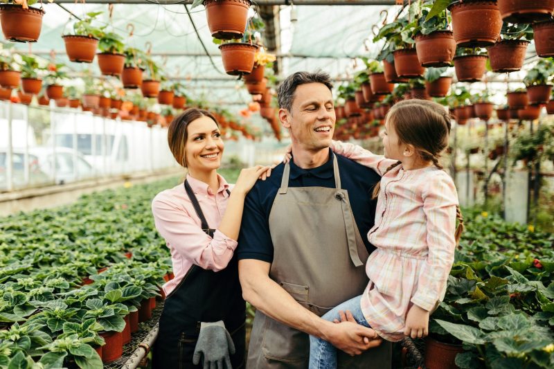 Happy parents talking to their small daughter while working at plant nursery.