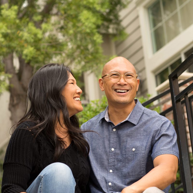 Portrait of an Asian couple smiling and hugging outside.