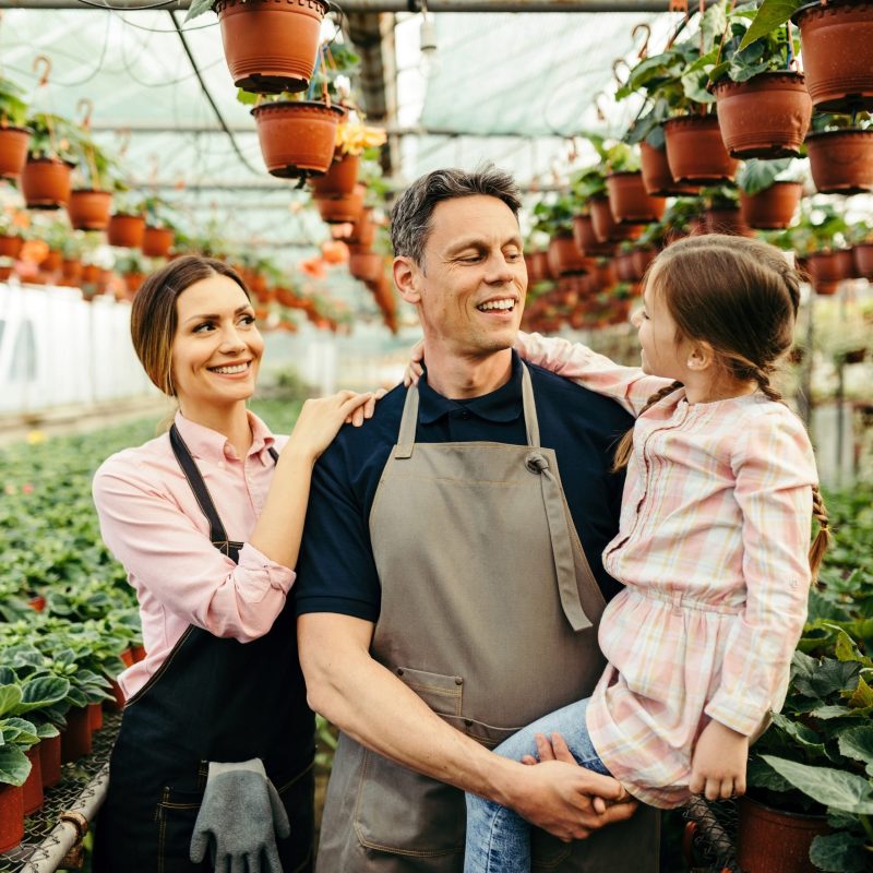 Happy parents talking to their small daughter while working at plant nursery.