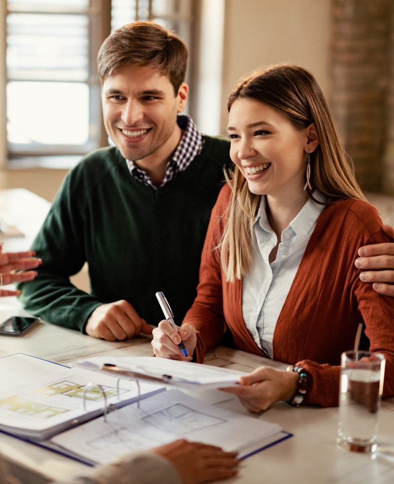 Young happy couple signing a contract while being on a meeting with insurance agent in the office.