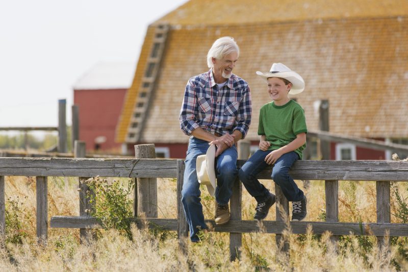 Grandfather and grandson sitting on fence beside barn